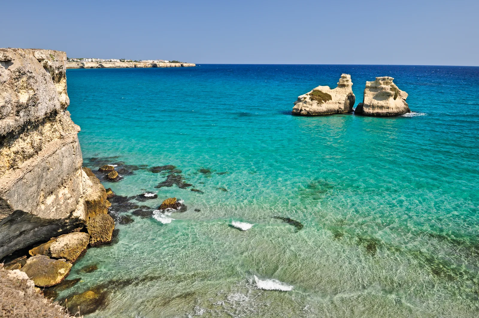 Costa rocciosa con mare cristallino turchese e i caratteristici faraglioni delle Due Sorelle