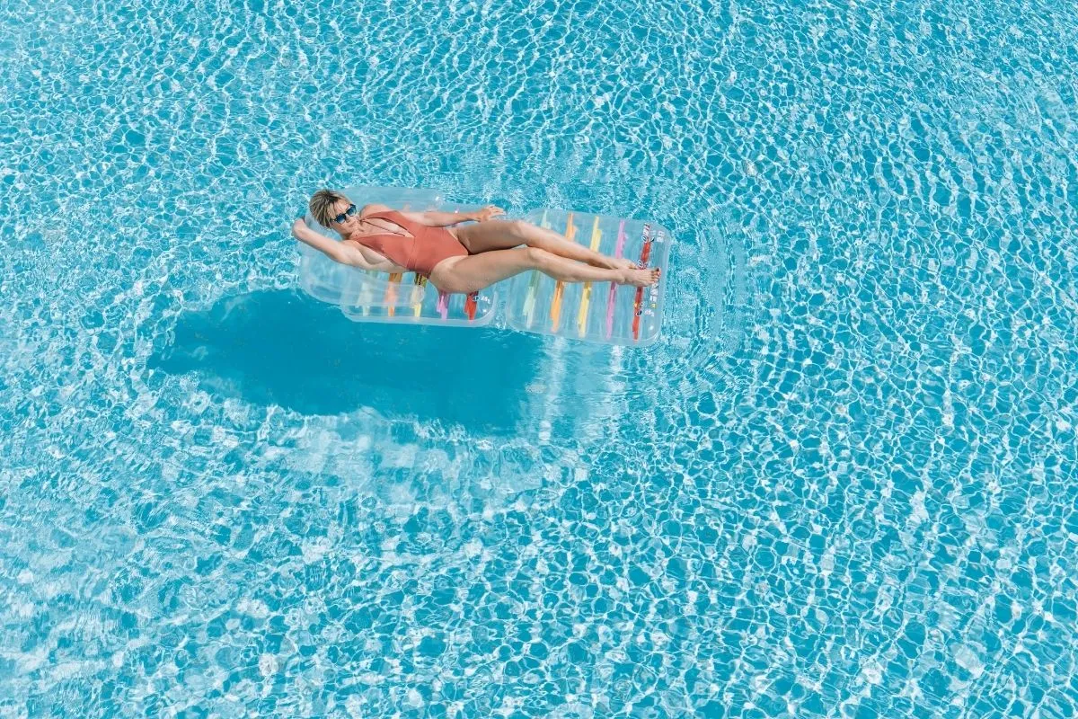 Donna che si rilassa su un materassino galleggiante in piscina dall'acqua cristallina