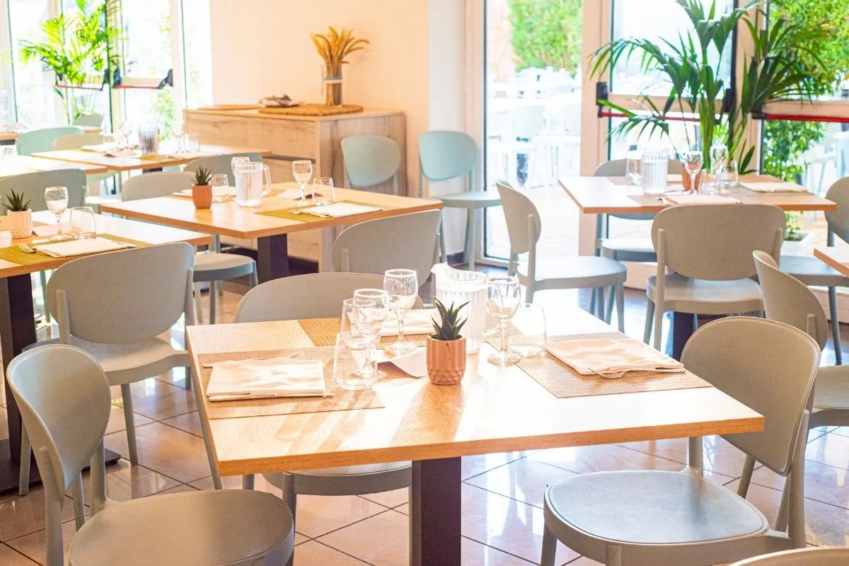 Sala ristorante luminosa con tavoli apparecchiati e piante verdi