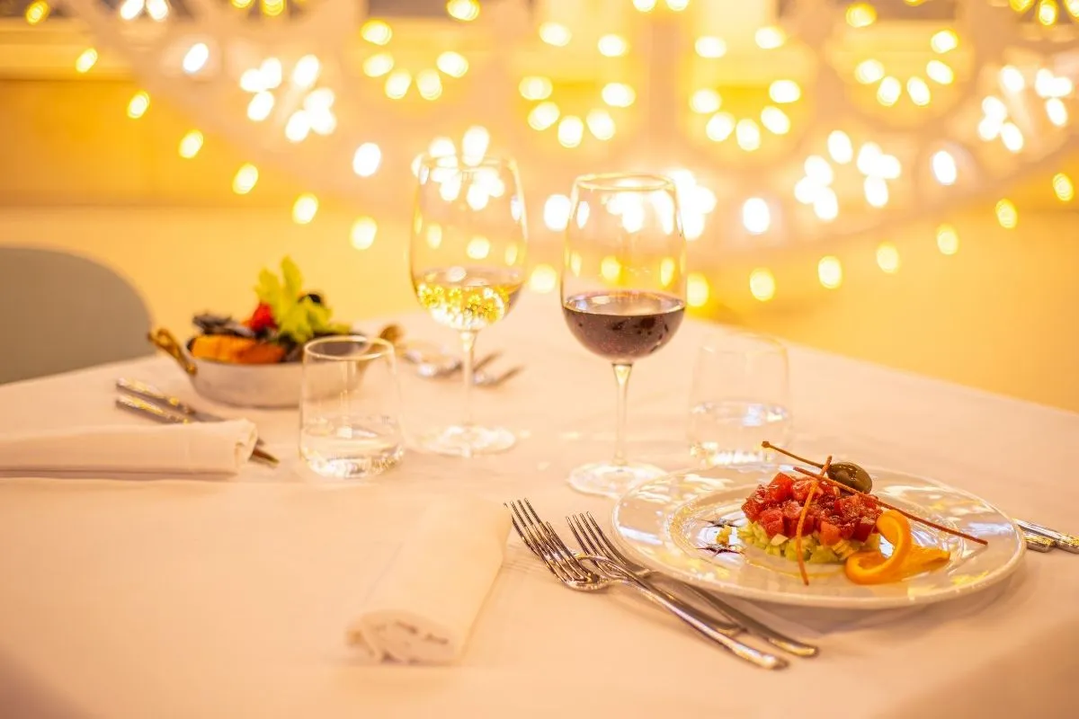 Tavolo elegante con tartare, calici di vino e luci soffuse sullo sfondo