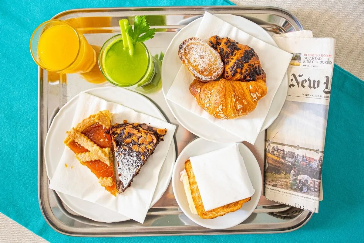 Vassoio di colazione con cornetti, crostate, succhi e quotidiano