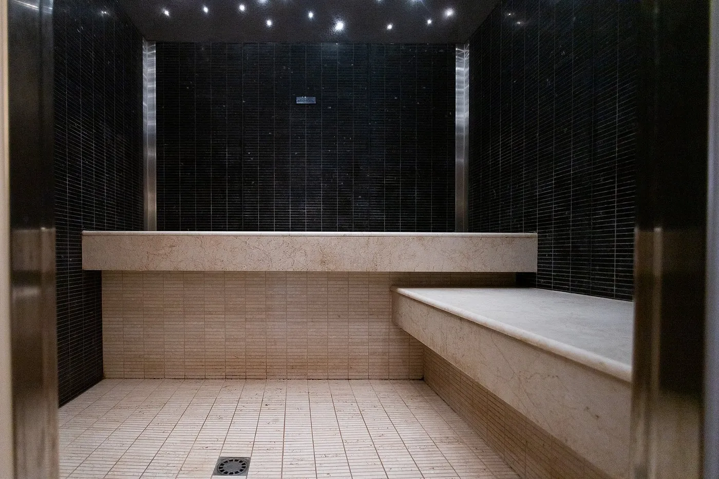 Bagno turco con rivestimento in mosaico nero e sedute in marmo chiaro