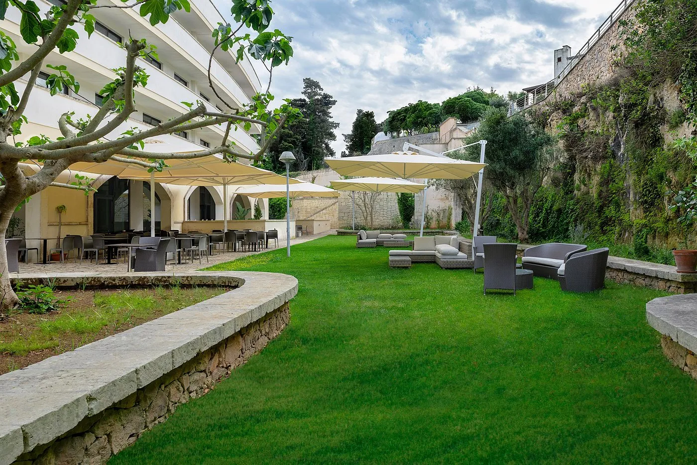 Giardino esterno con prato verde, area lounge, ombrelloni e parete rocciosa
