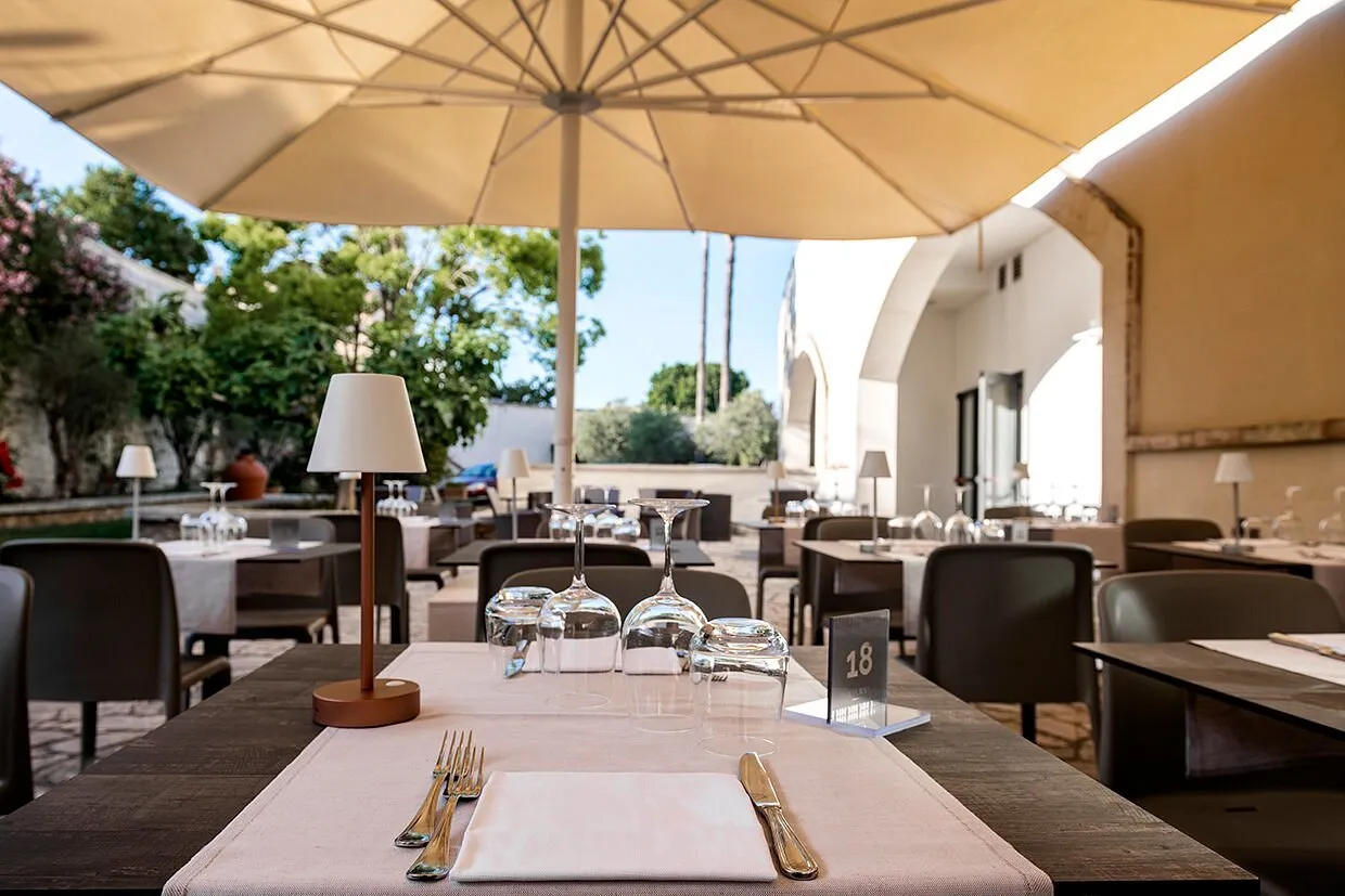 Ristorante esterno sotto ombrelloni con tavoli apparecchiati e portico ad archi