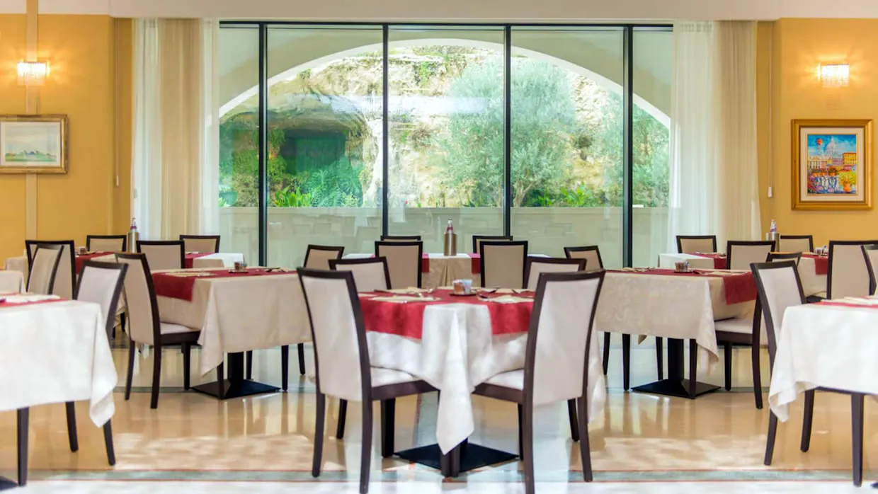 Sala ristorante interna con tavoli apparecchiati e grande vetrata sul giardino roccioso