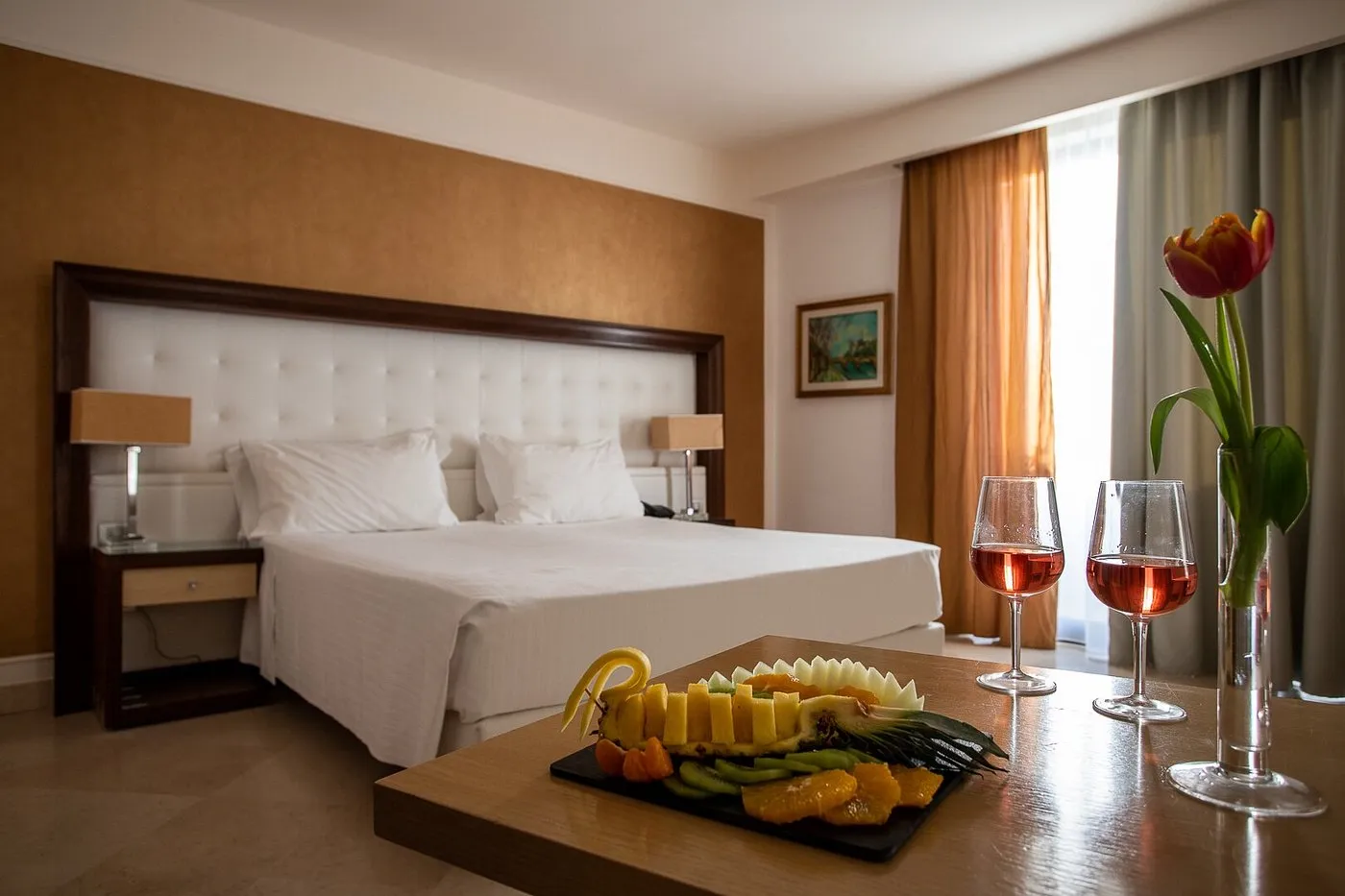 Camera matrimoniale con testiera bottonata bianca e tavolo con piatto di frutta e vino