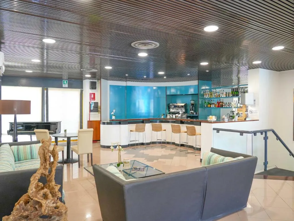 Hall con bancone bar azzurro, sgabelli, divani grigi e pianoforte a coda