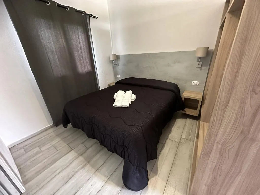 Camera matrimoniale con letto scuro, comodini e tende grigie