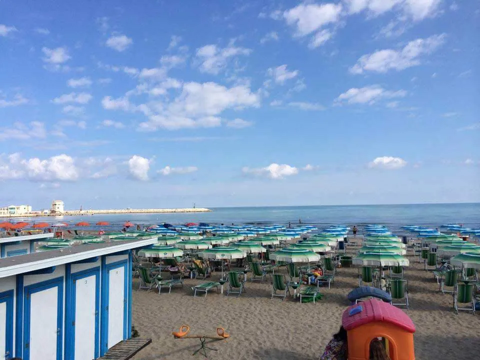 Spiaggia sabbiosa con file di ombrelloni colorati e mare azzurro