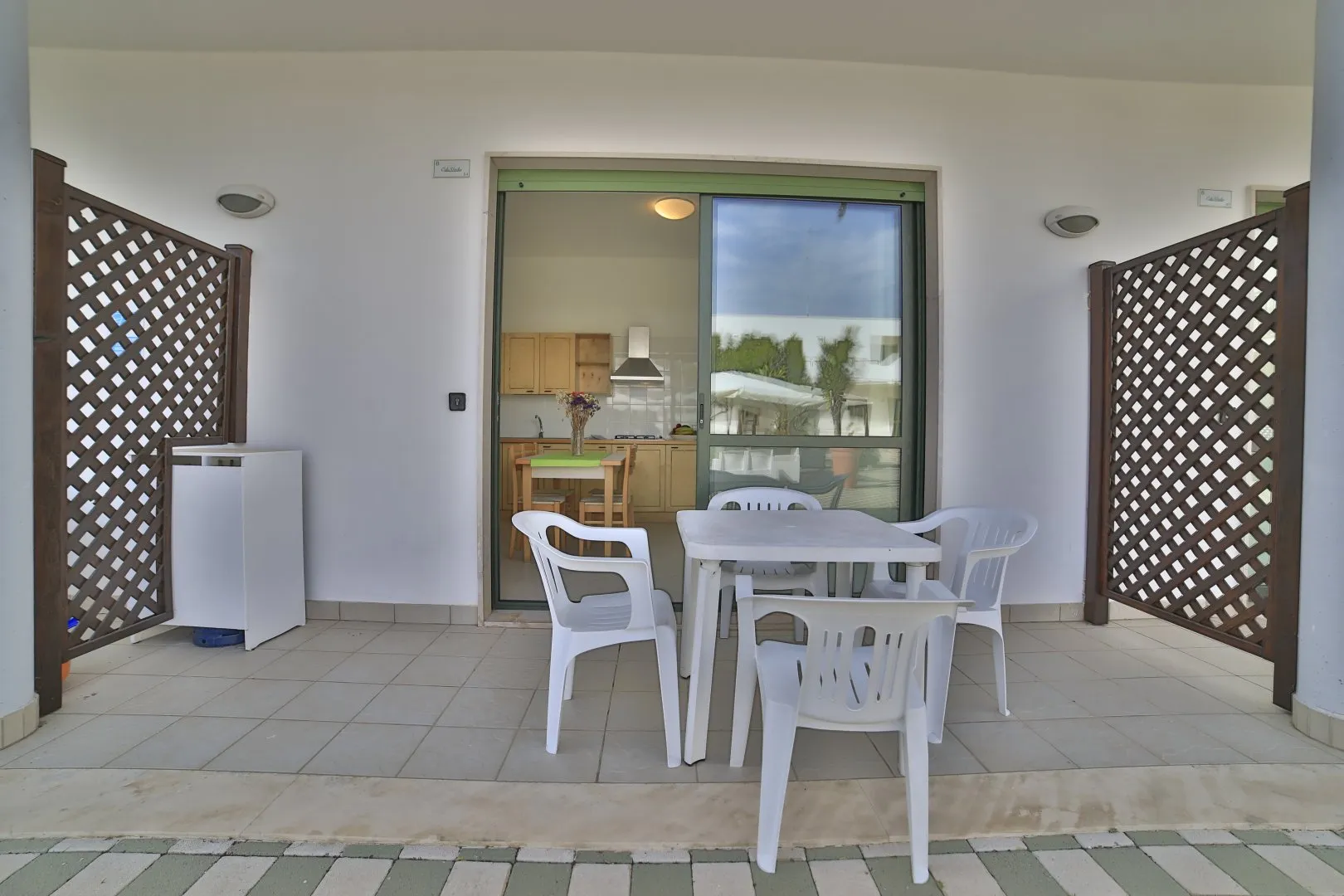 Veranda esterna con tavolo e sedie bianche e affaccio sulla cucina