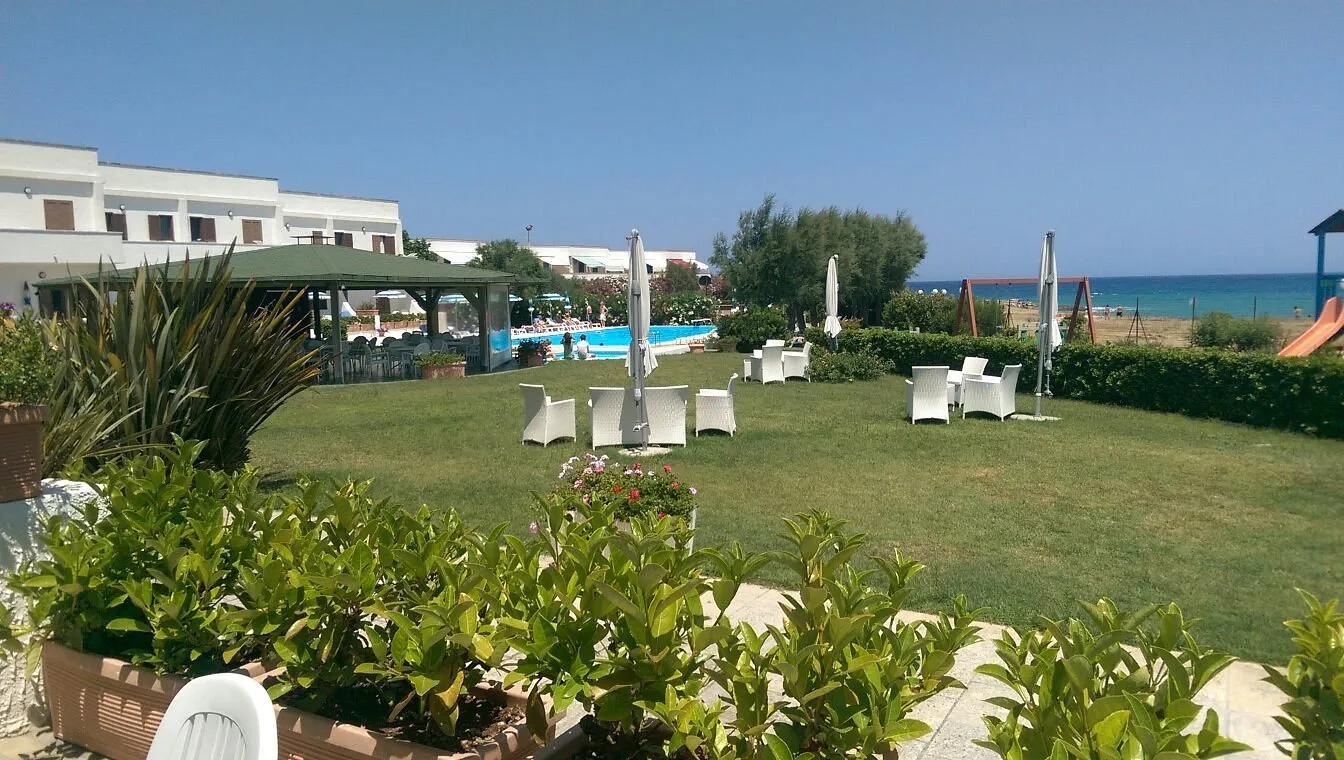 Giardino con poltrone bianche e ombrelloni, area piscina e mare sullo sfondo