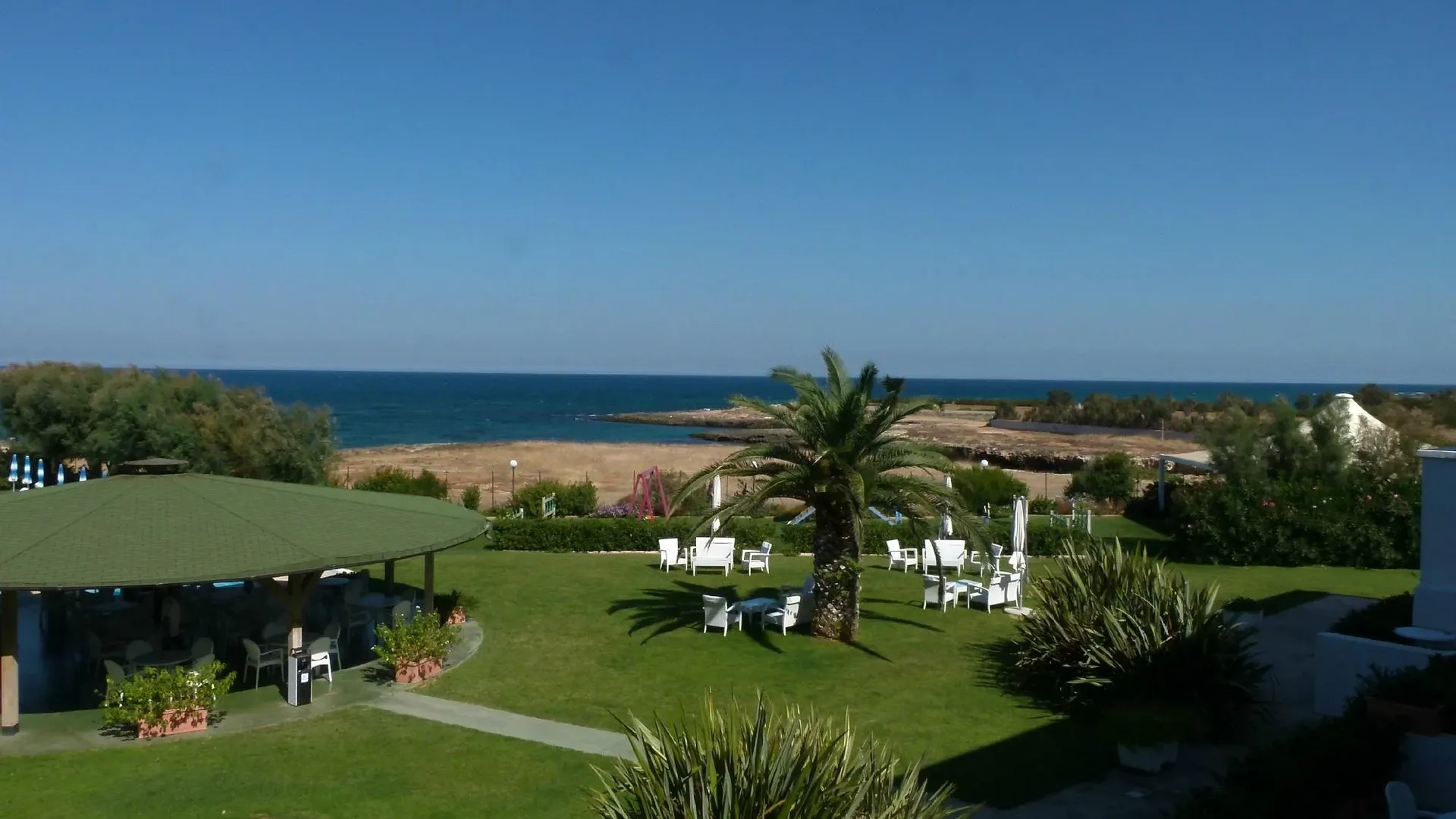 Panorama del giardino con gazebo verde, palma e poltrone bianche affacciato sul mare
