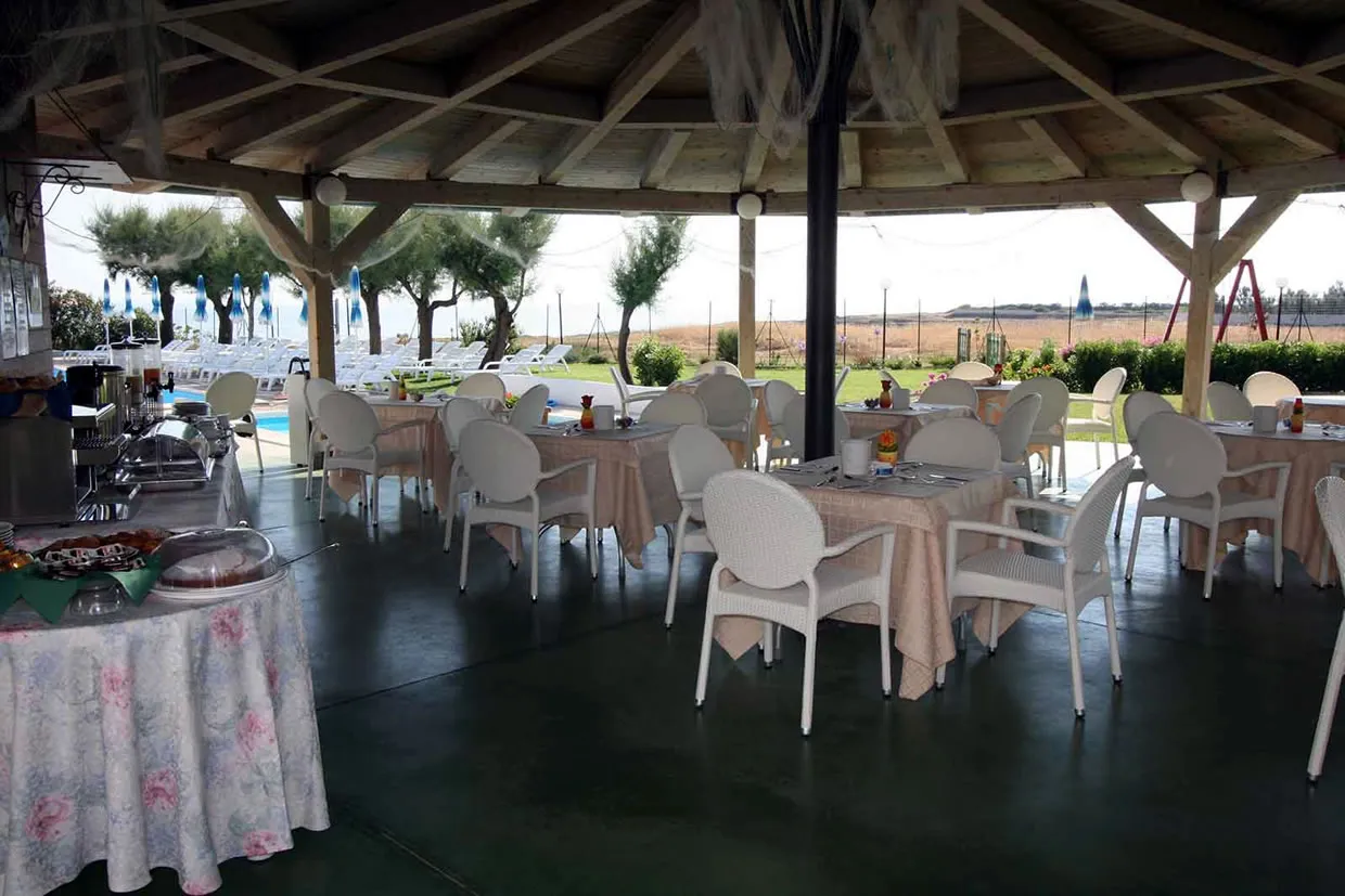 Sala ristorante coperta da gazebo in legno con tavoli e sedie bianche e buffet per la colazione