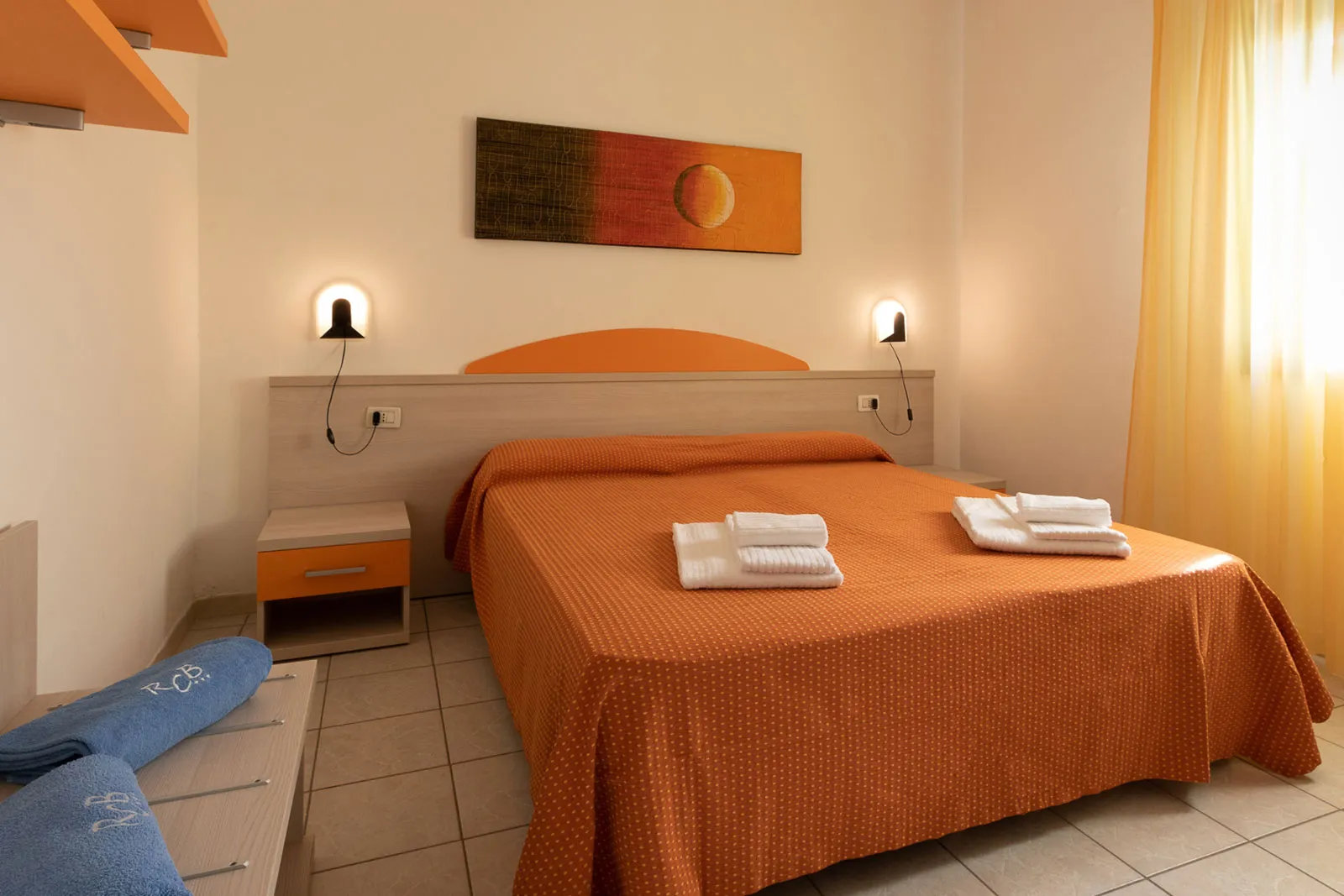 Camera da letto matrimoniale con copriletto arancione e luci da lettura