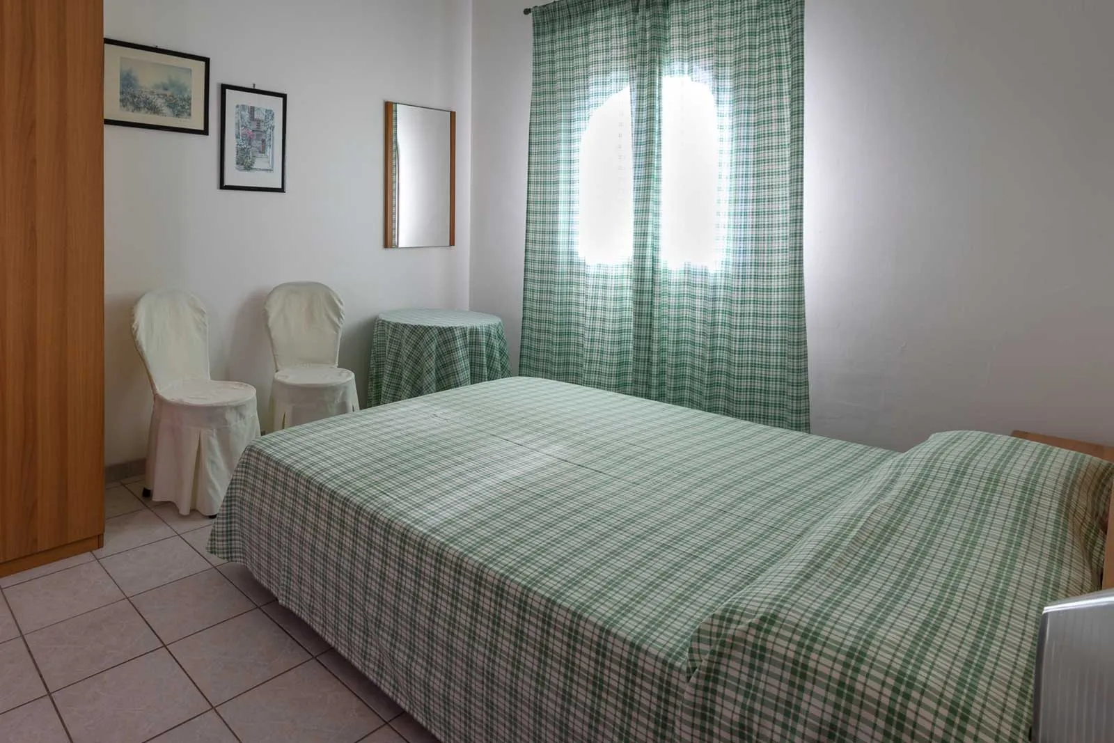 Camera da letto matrimoniale con copriletto a quadri verdi e sedie bianche