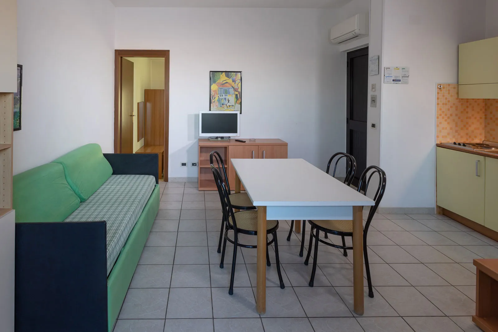Soggiorno con angolo cottura, divano verde, tavolo da pranzo e TV