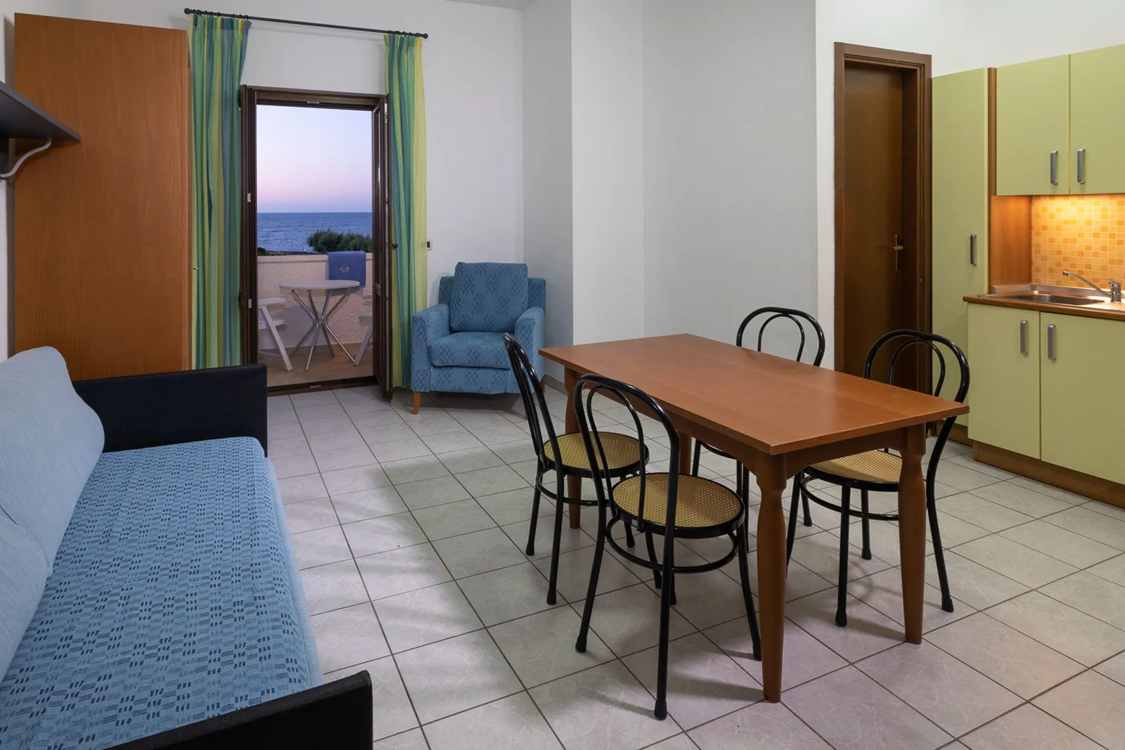 Soggiorno con angolo cottura, divano e tavolo da pranzo con porta finestra affacciata sul mare