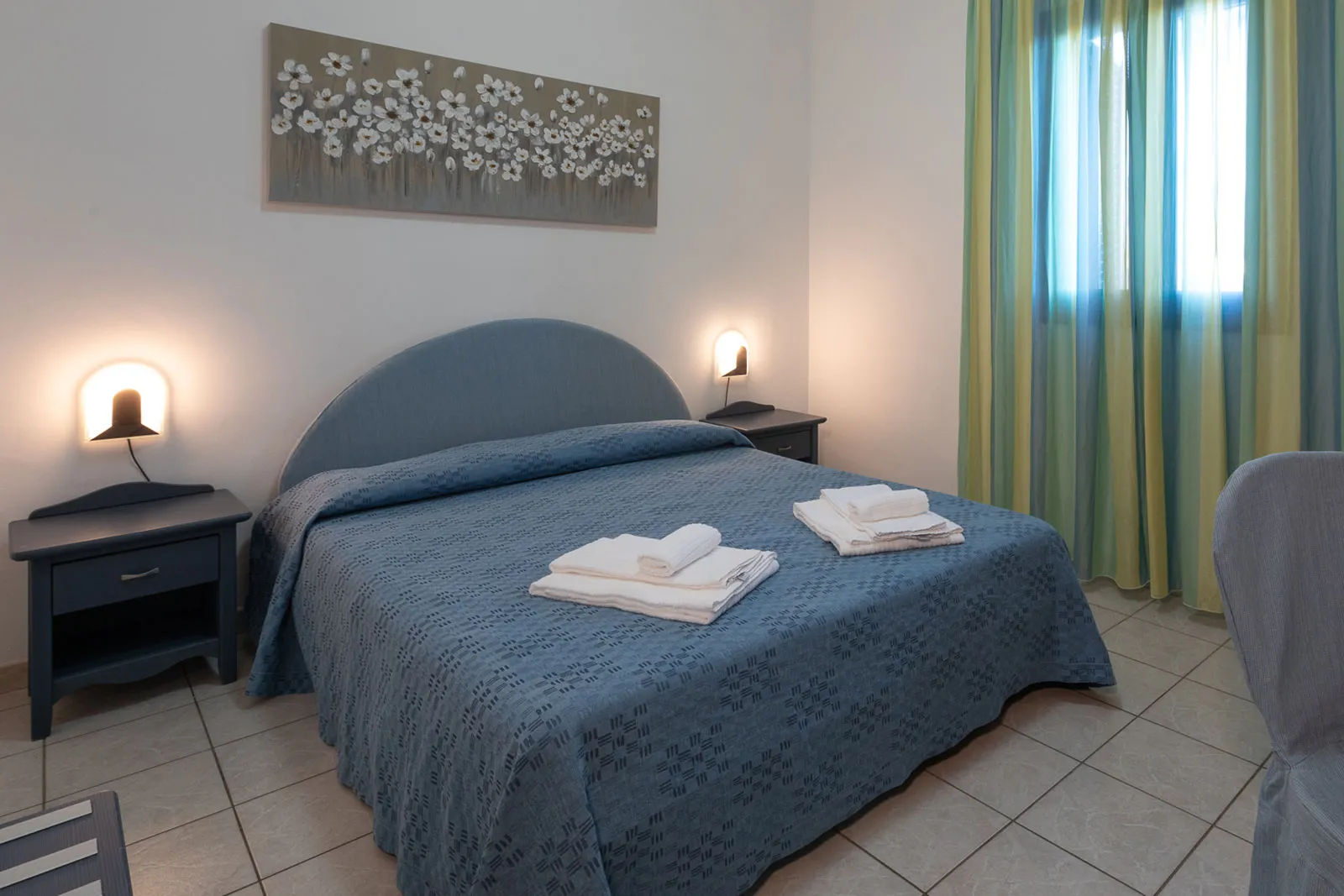 Camera da letto matrimoniale con copriletto blu e quadro floreale