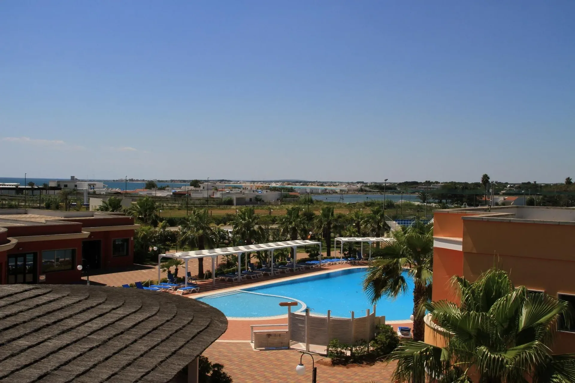 Vista panoramica del resort con piscina, palme ed edifici, mare all'orizzonte