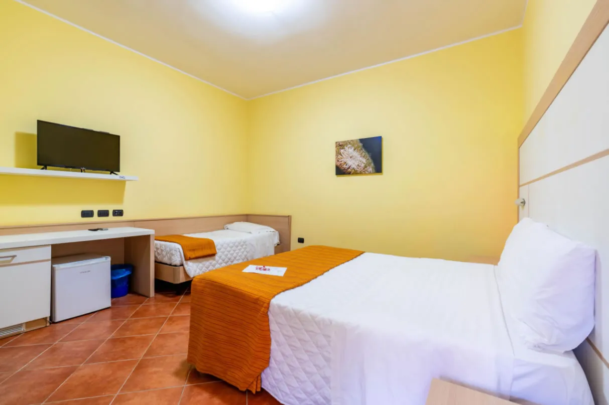 Camera con letto matrimoniale e letto singolo, pareti gialle, TV e scrivania