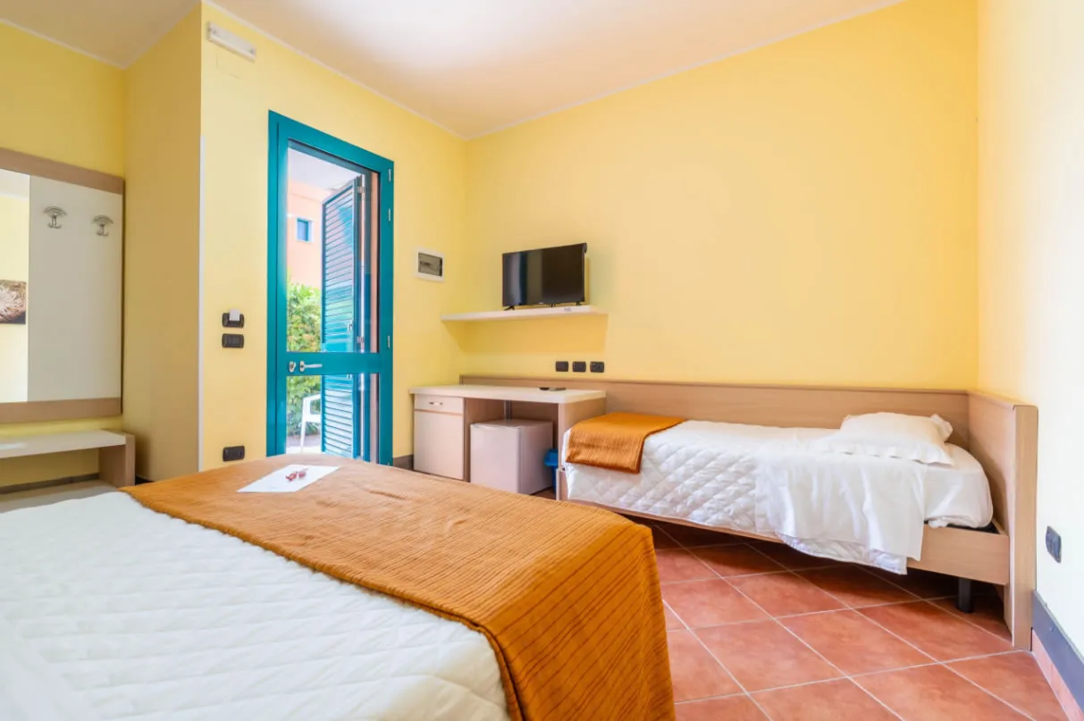 Camera con letto matrimoniale e singolo, porta-finestra aperta sul giardino