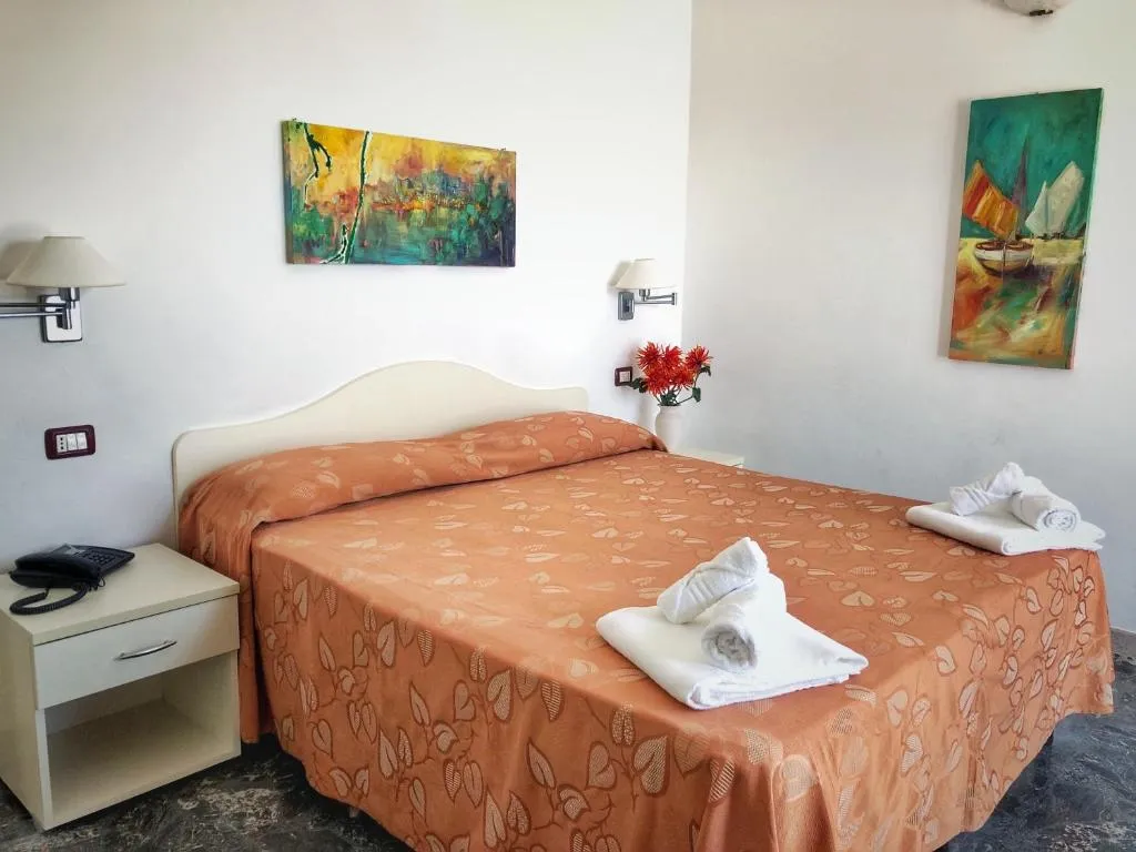 Camera con letto matrimoniale, copriletto arancione, asciugamani e quadri marini