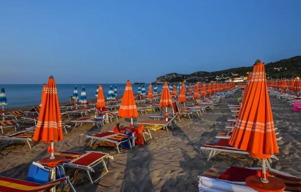 Spiaggia attrezzata con ombrelloni arancioni e azzurri al crepuscolo