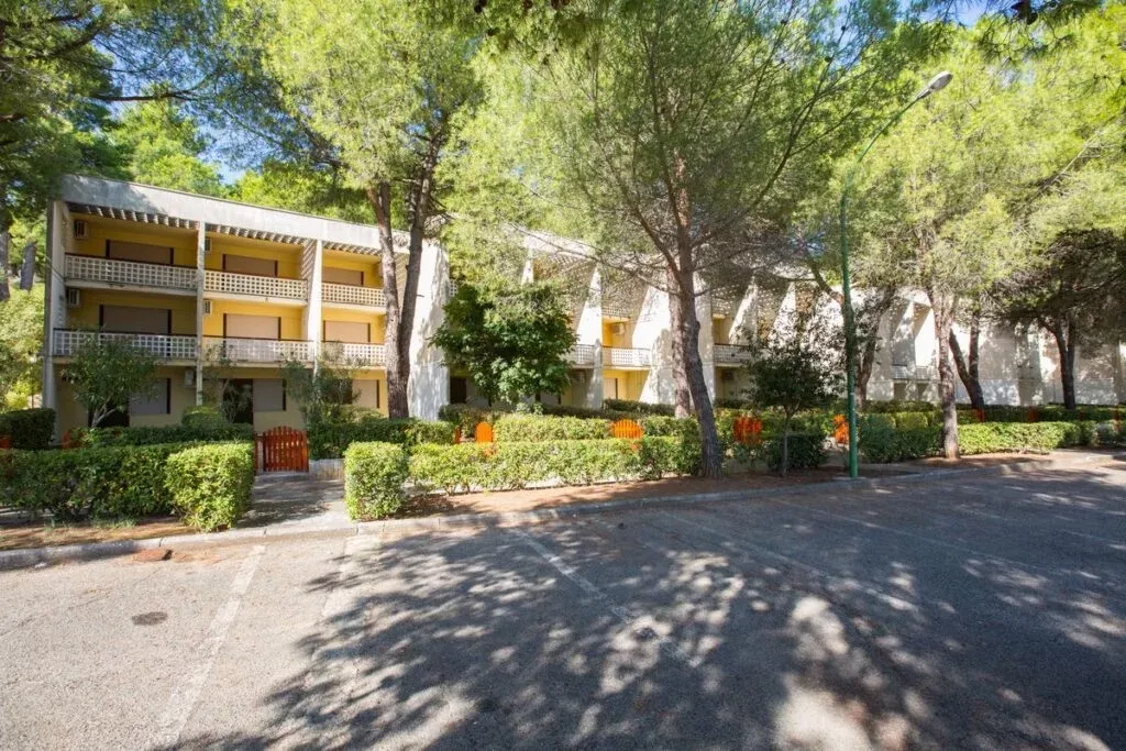 Edificio residenziale giallo con balconi circondato da pini e parcheggio