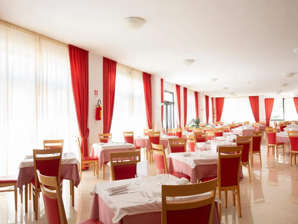 Sala ristorante luminosa con tavoli apparecchiati e tende rosse