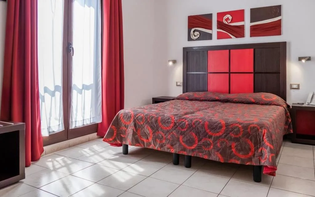 Camera matrimoniale luminosa con tende rosse, testiera rossa e nera e pavimento chiaro