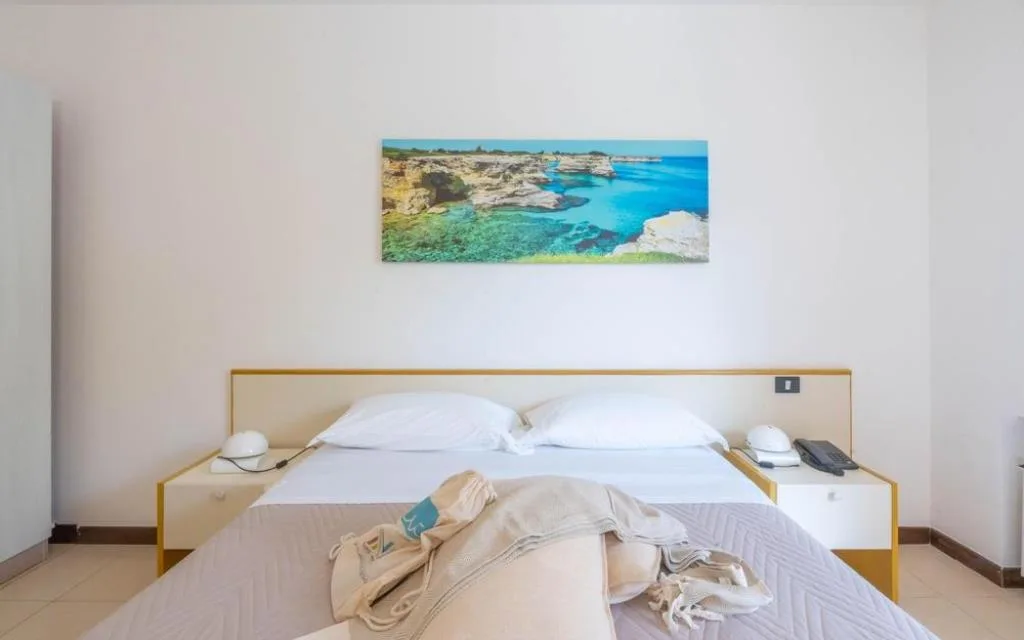 Letto matrimoniale con quadro panoramico del mare e comodini bianchi