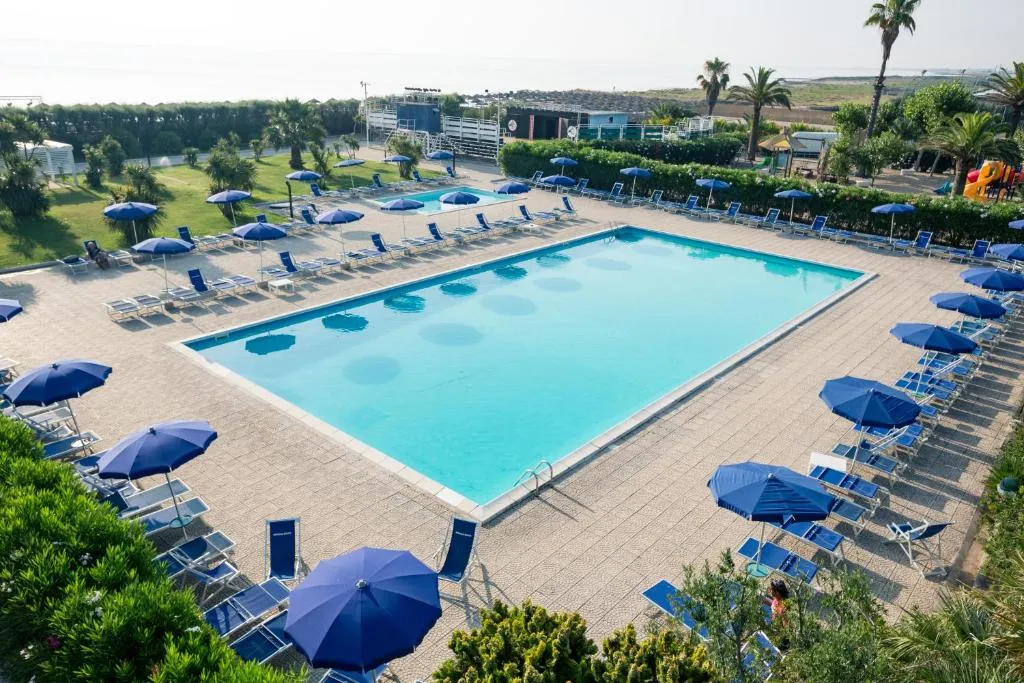 Grande piscina con ombrelloni e lettini blu e vista sul mare in lontananza