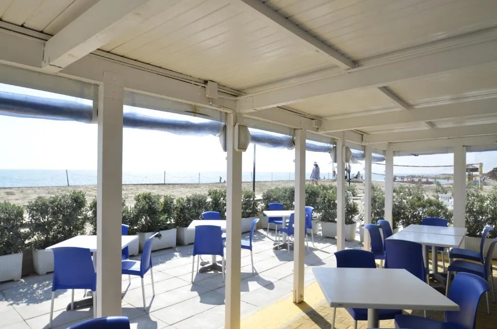 Terrazza coperta con tavoli e sedie blu affacciata sulla spiaggia e il mare