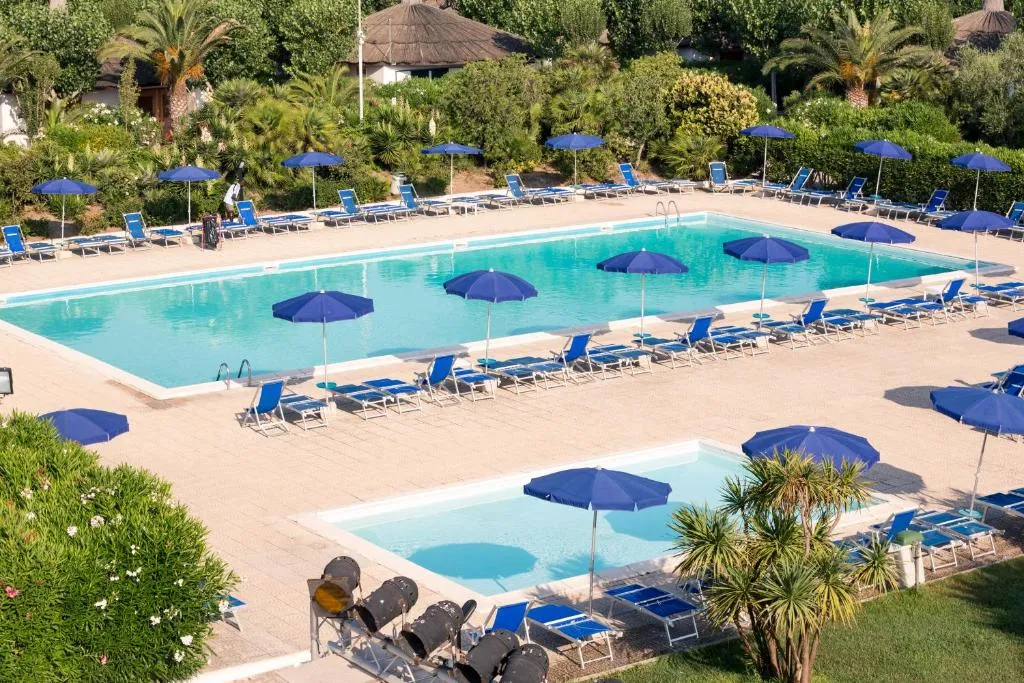 Due piscine con ombrelloni blu e lettini circondate da giardino e vegetazione