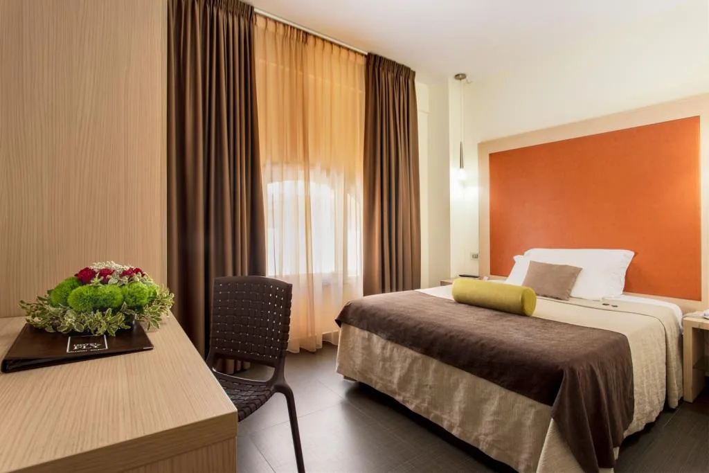Camera con scrivania, sedia, composizione floreale e letto con testiera arancione