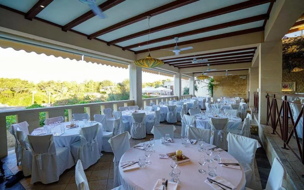 Sala ristorante esterna con tavoli rotondi apparecchiati e vista sul verde