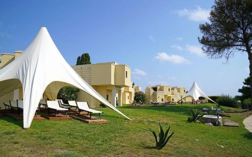Giardino esterno con tende bianche, lettini e ville in pietra