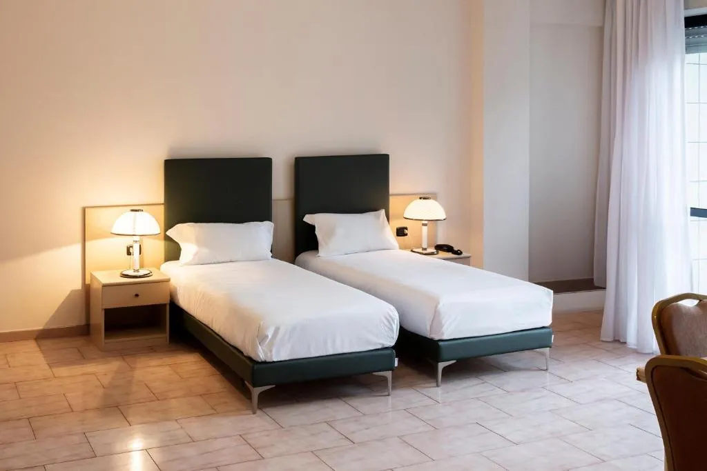 Camera con due letti singoli, lampade da comodino e pavimento chiaro