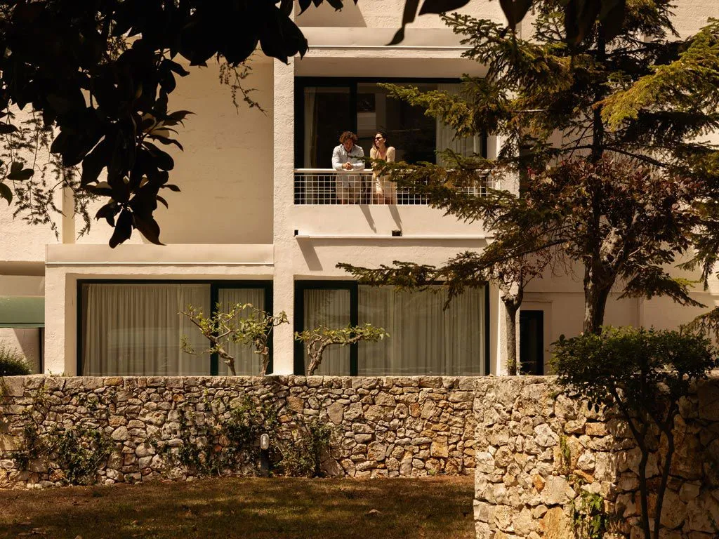 Ospiti affacciati dal balcone di una camera con muro in pietra e vegetazione