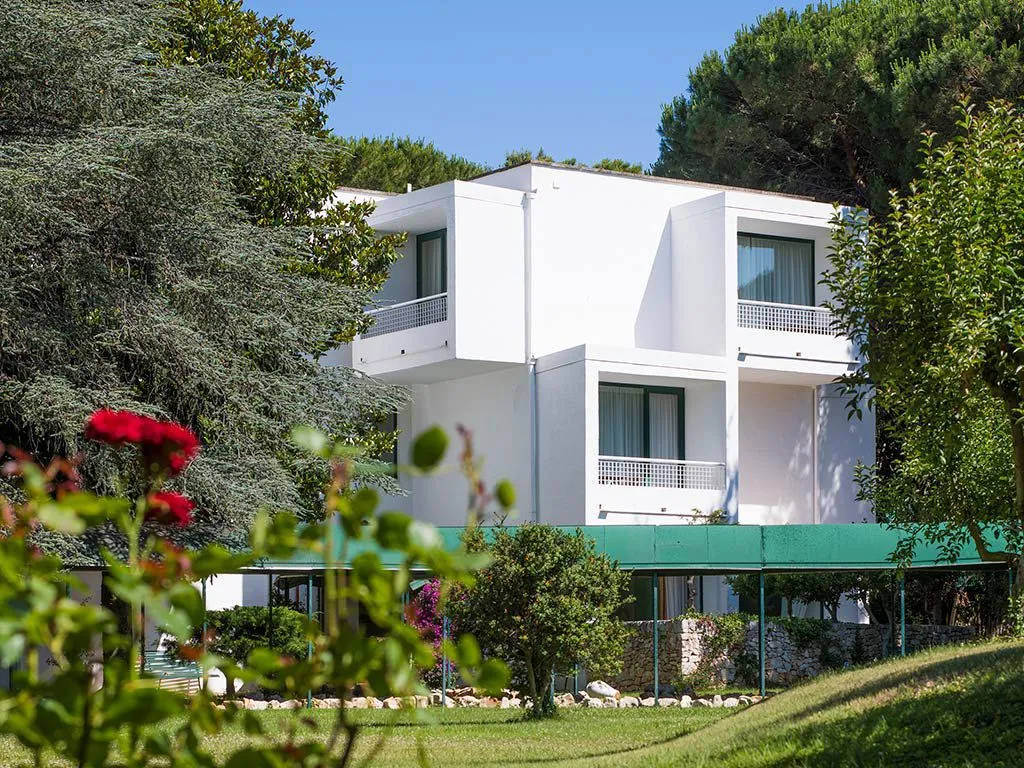 Edificio bianco dell'hotel con balconi circondato da alberi e fiori rossi