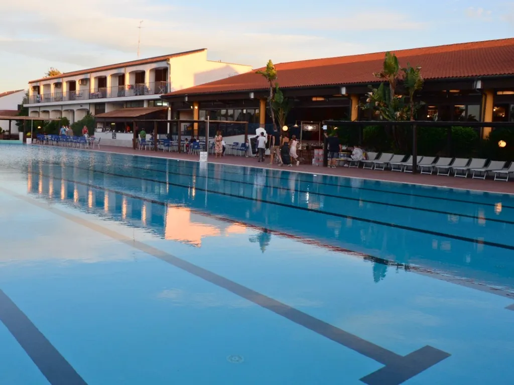 Piscina al tramonto con bar e zona ristoro affollata sul bordo