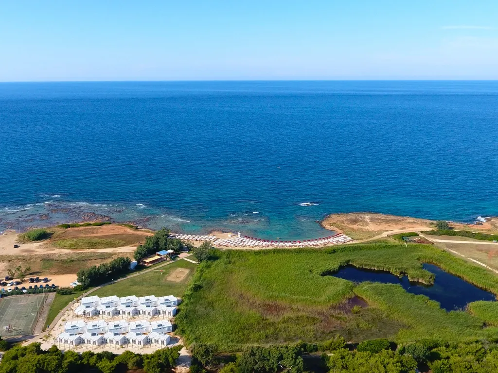 Panorama aereo della costa con mare blu, spiaggia attrezzata e bungalow