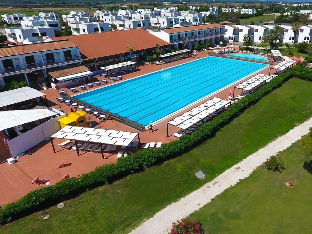 Vista aerea della grande piscina con lettini e edifici bianchi del resort