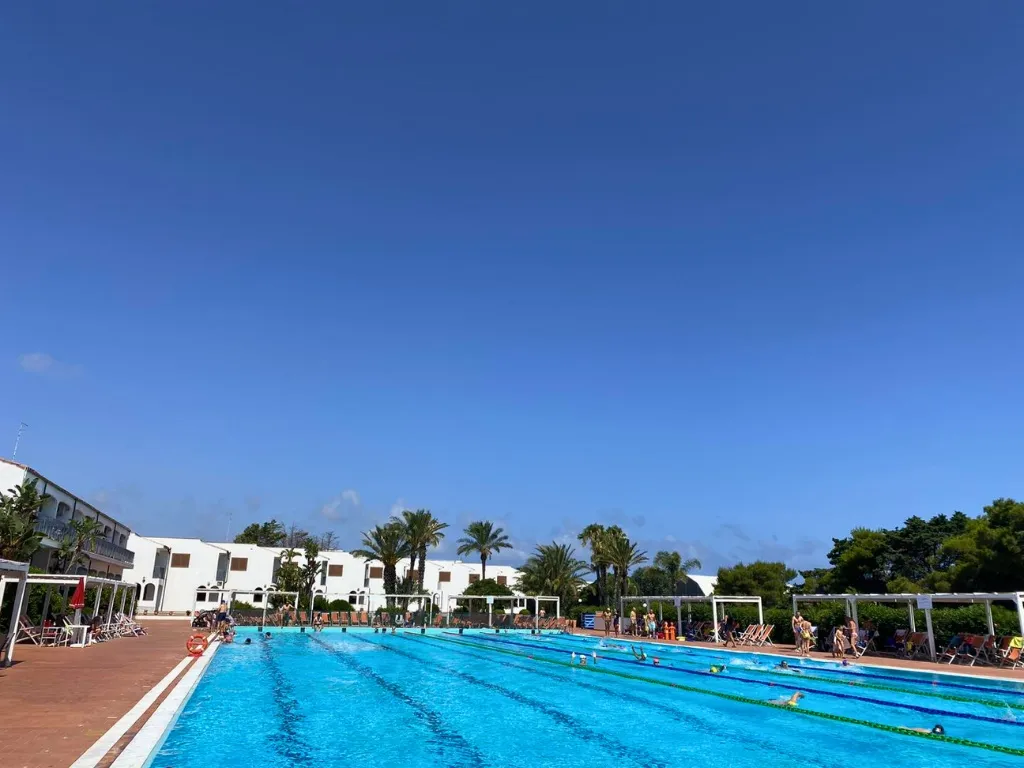 Piscina con corsie e bagnanti circondata da edifici bianchi e palme