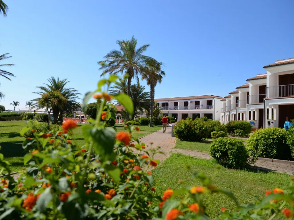 Giardino fiorito con palme e camminamento tra gli edifici del resort