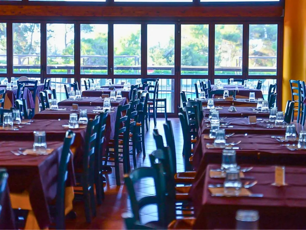 Sala da pranzo con grandi vetrate affacciate sul verde e tavoli apparecchiati