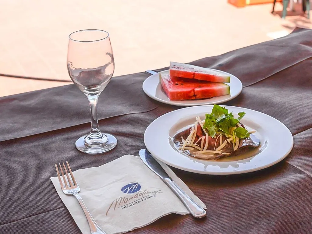 Tavolo apparecchiato con piatto gourmet, anguria e calice di vino