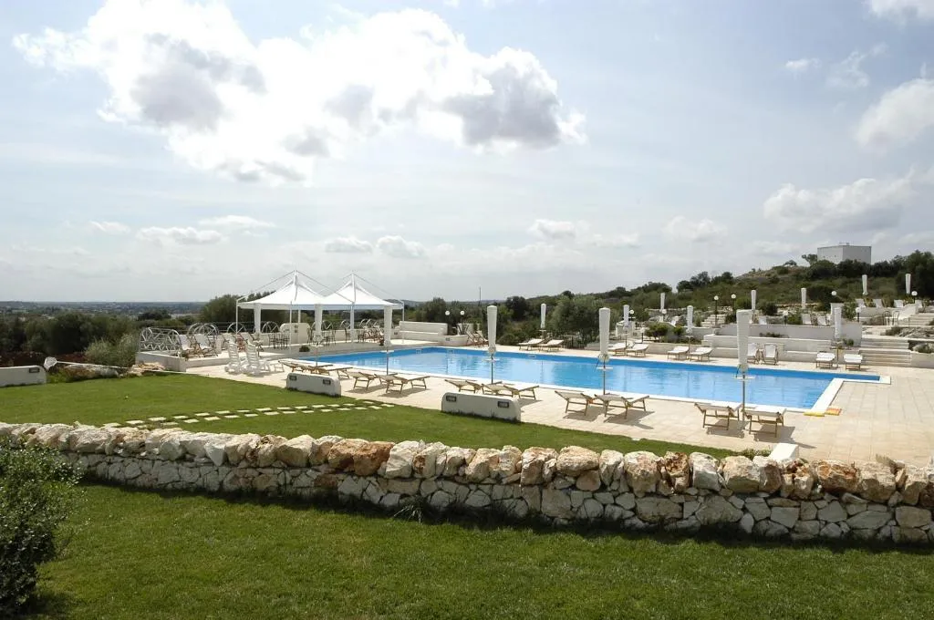 Ampia piscina diurna con gazebo bianchi, lettini e muretto in pietra