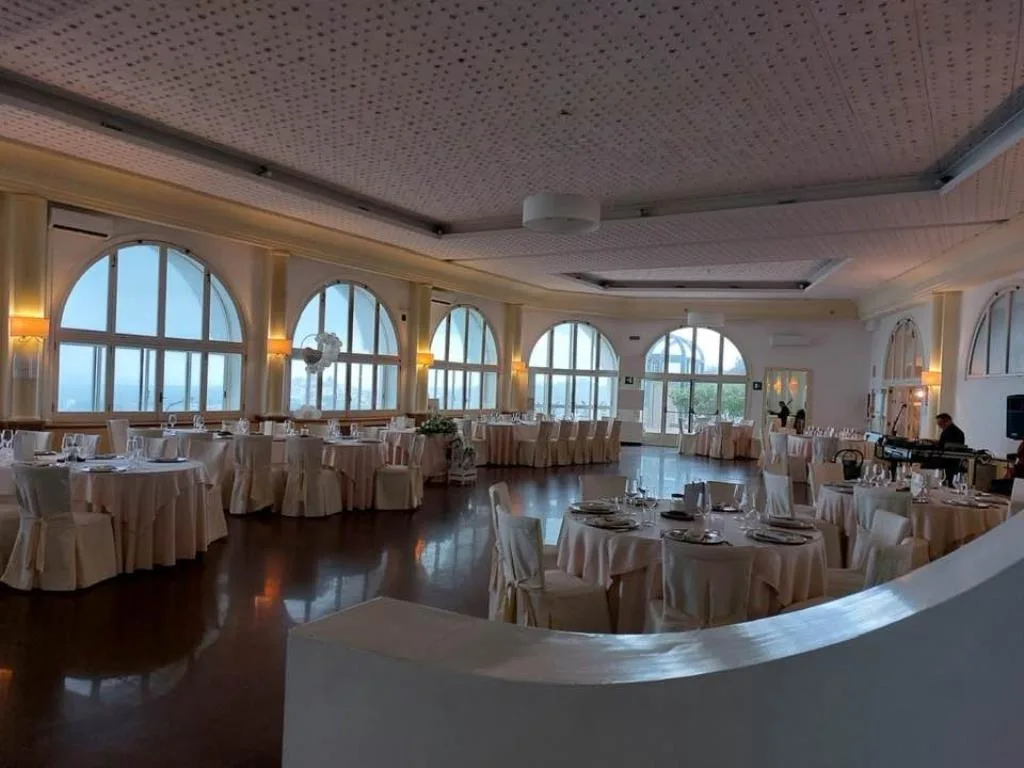 Ampia sala banchetti elegante con tavoli rotondi e finestre arcuate