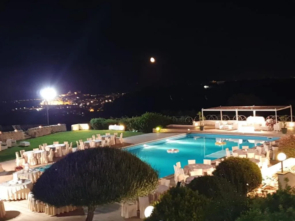 Piscina illuminata di notte con tavoli allestiti e vista sulle luci della città